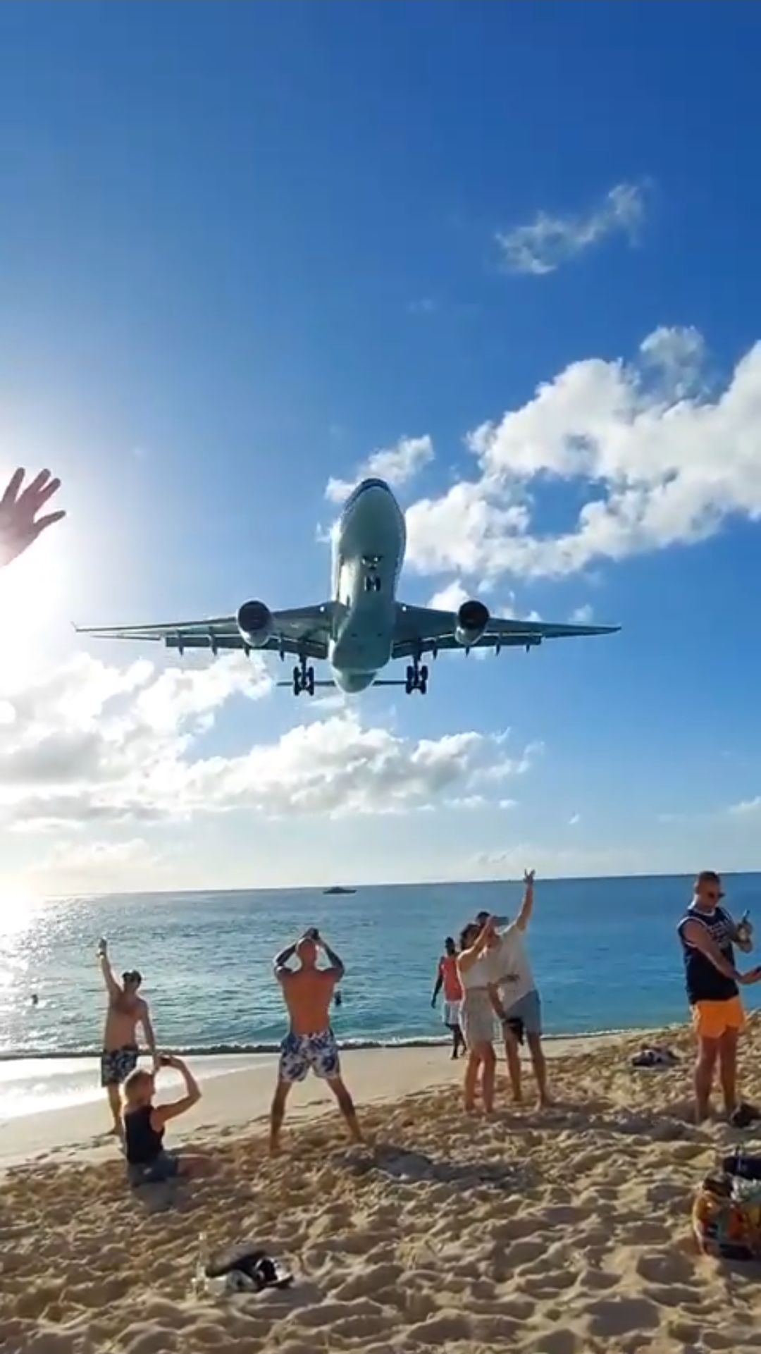 A jet landing low over Maho Beach, St. Maarten, as guests wave and take photos